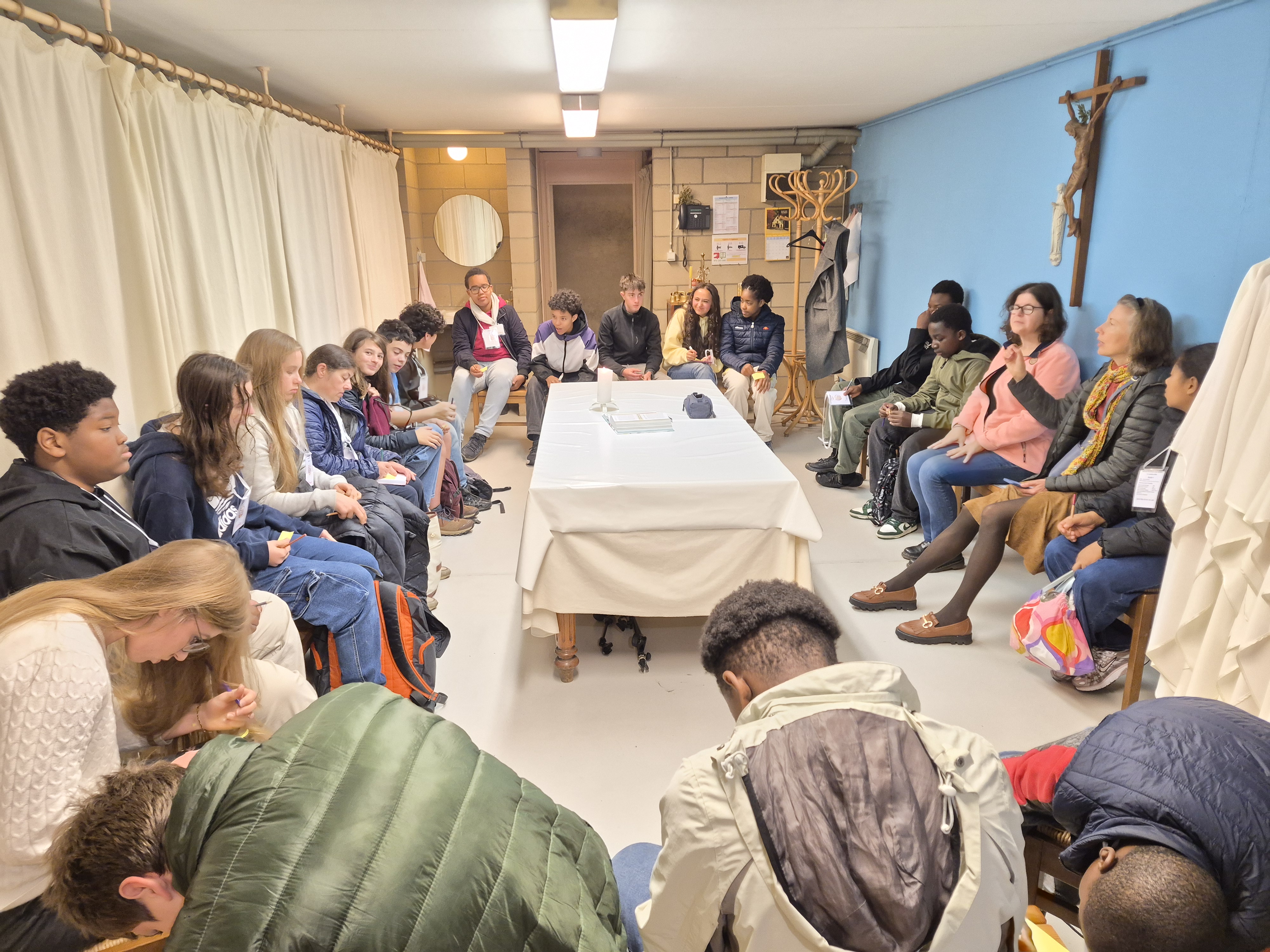 Assis en cercle autour d'une table, dans une petite salle, des jeunes acolytes en tenue de tous les jours écoutent une animatrice lors d'un atelier